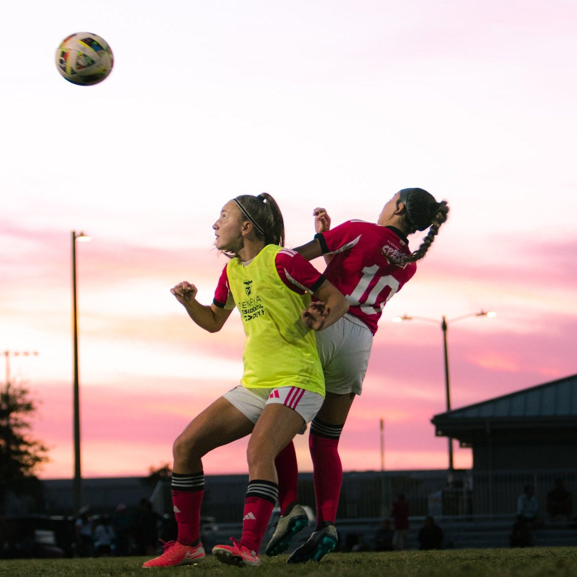 Two female soccer players competing for the ball during a sunset match.
