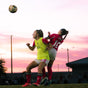Two female soccer players competing for the ball during a sunset match.